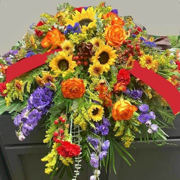 Colorful floral casket spray with sunflowers, orange roses, and purple blooms