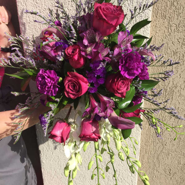 Handheld bouquet of pink roses and purple flowers with trailing white blooms