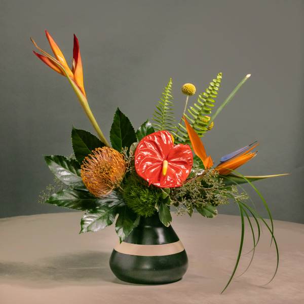 Tropical floral arrangement in a dark vase with orange and red blooms