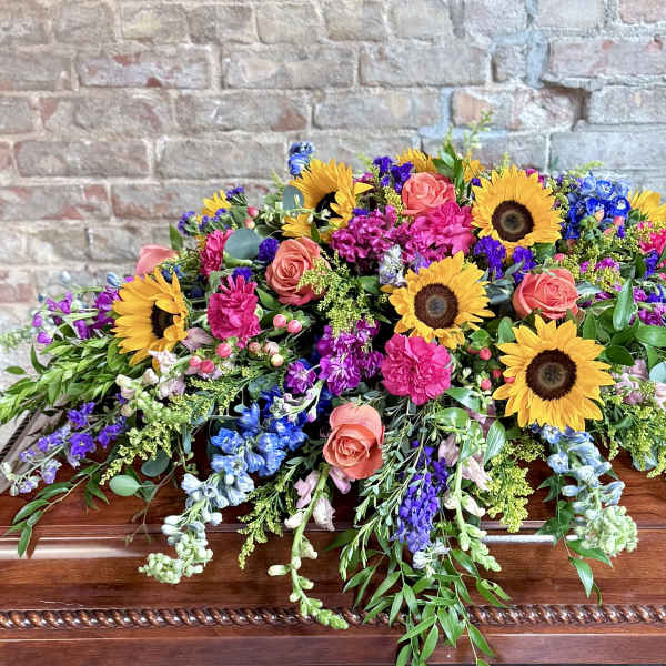 Colorful floral casket spray with sunflowers, roses, and purple blooms