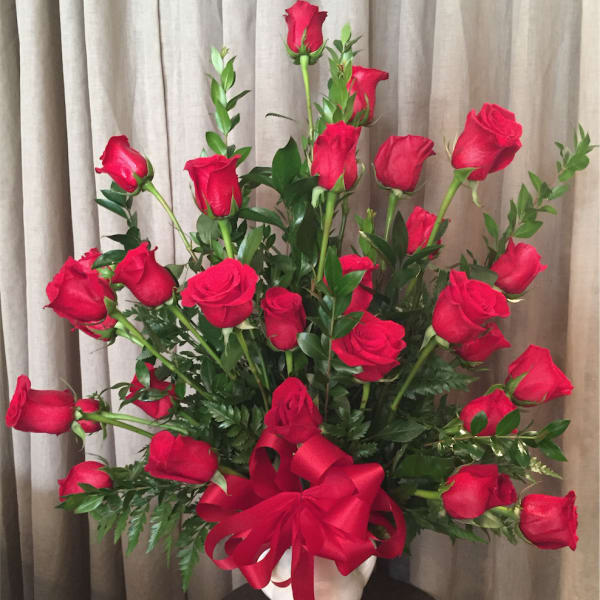 Red roses arranged in a white vase with a red ribbon bow