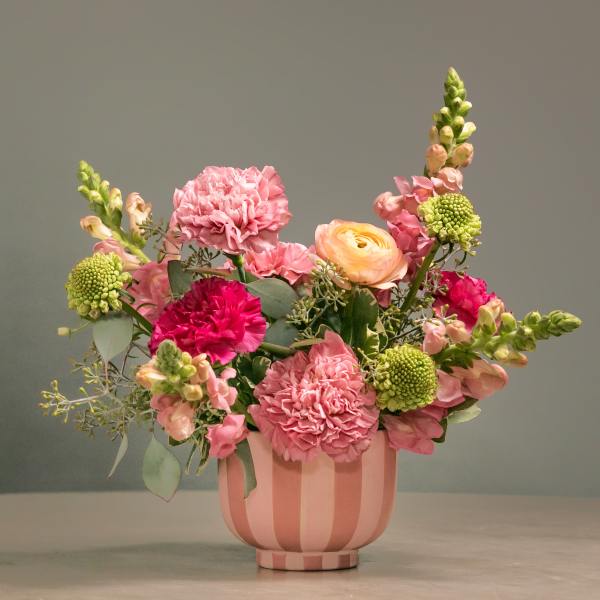 Pink and peach mixed flower arrangement in a striped pink vase