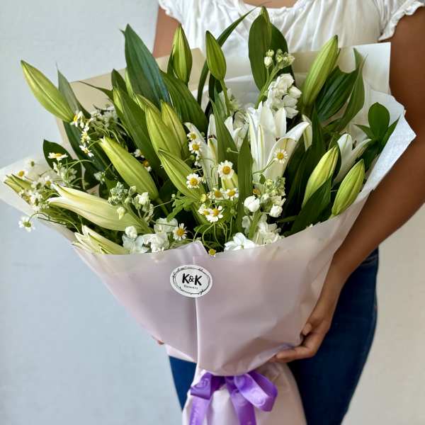 Bouquet of white lilies and small white daisies wrapped in pale pink paper