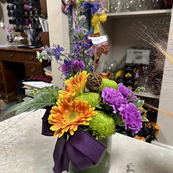 Colorful bouquet in a glass vase with orange gerberas, green mums, and purple carnations