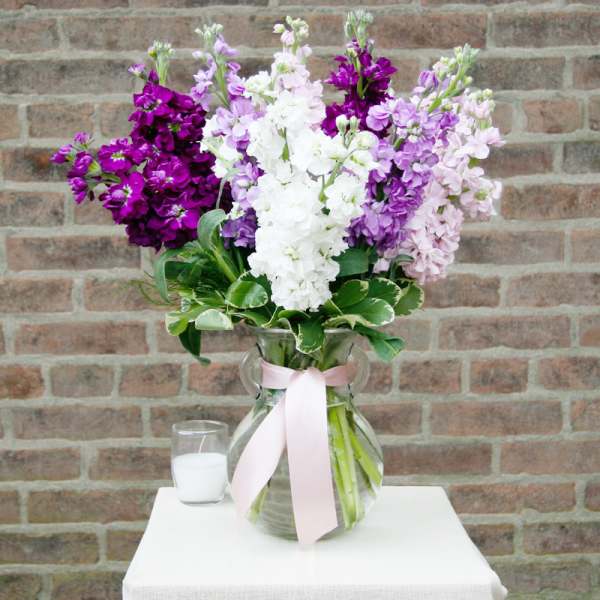 Bouquet of purple, pink, and white flowers in a glass vase with a ribbon