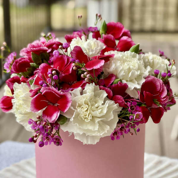 Pink and white carnations with small purple flowers in a pink box
