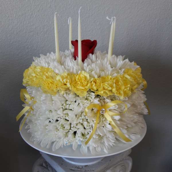 White and yellow floral arrangement with red roses and tall white candles
