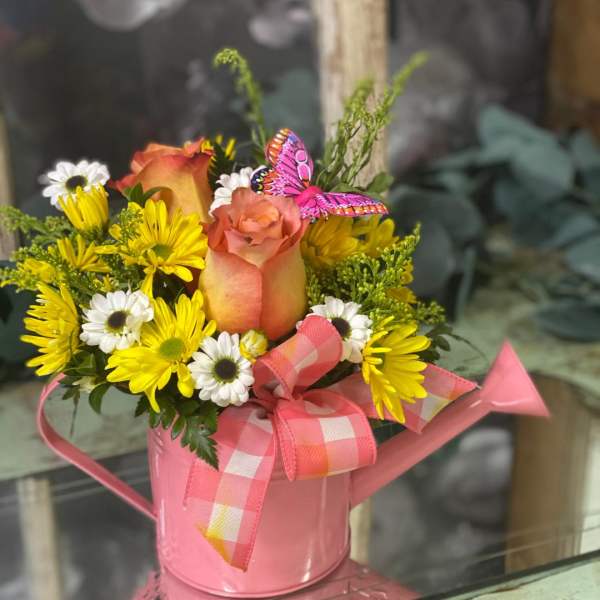Pink watering can holding yellow and white flowers with a rose and ribbon