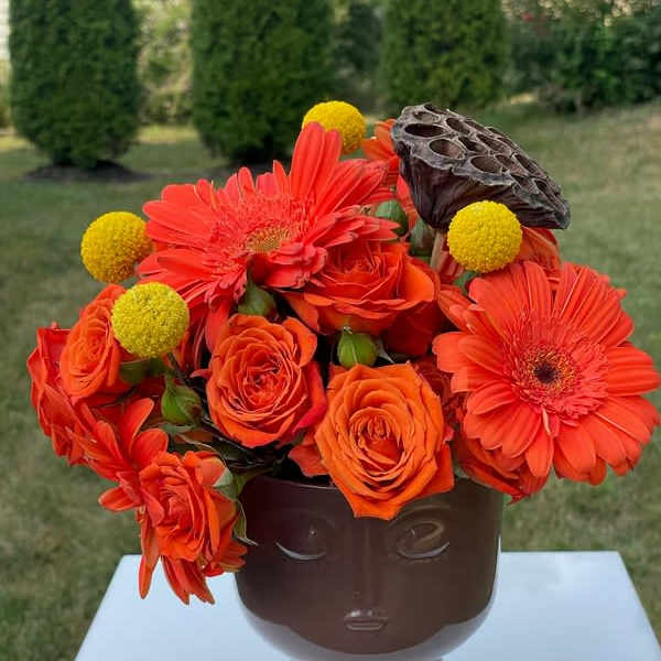 Orange roses and gerbera daisies in a brown face vase