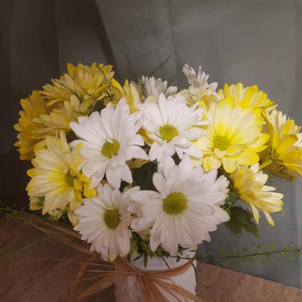 Yellow and white daisy bouquet in a white vase with a ribbon