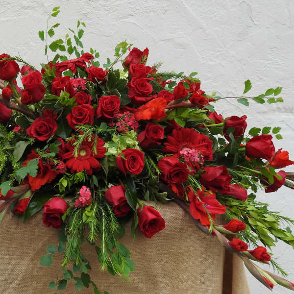 Large red rose arrangement with mixed greenery on a burlap-draped stand