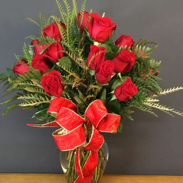 Red roses arranged in a glass vase with a red ribbon bow