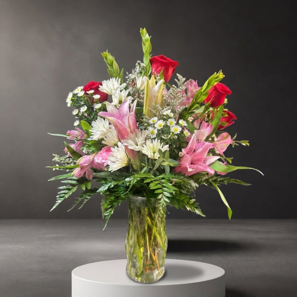 Mixed bouquet of red roses, pink lilies, and white daisies in a glass vase