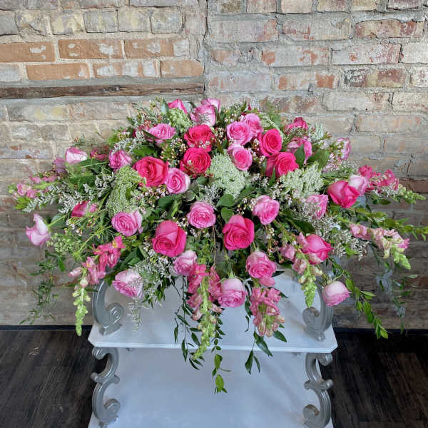 Large pink rose arrangement with trailing greenery on a white pedestal