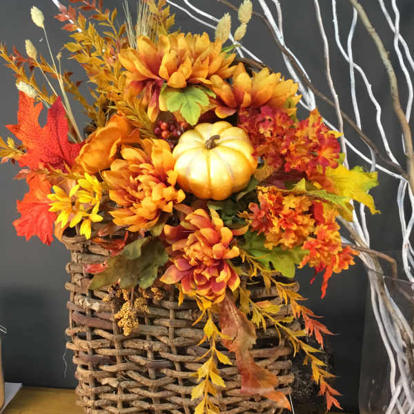 Autumn floral arrangement in a woven basket with orange flowers and a small pumpkin