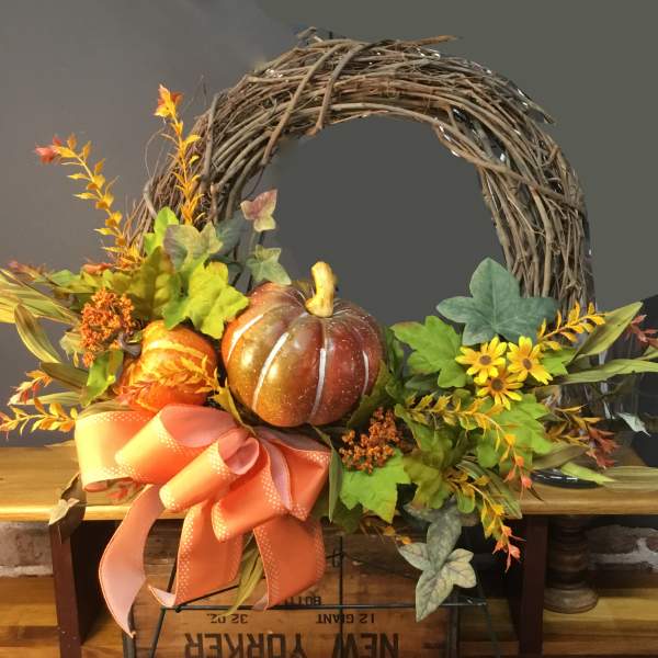 Fall wreath with pumpkins, yellow flowers, and a large orange ribbon
