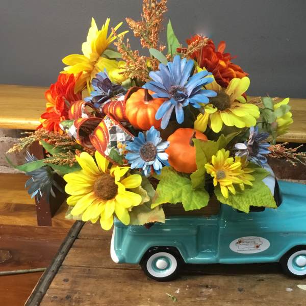 Fall floral arrangement in a turquoise truck-shaped container with pumpkins
