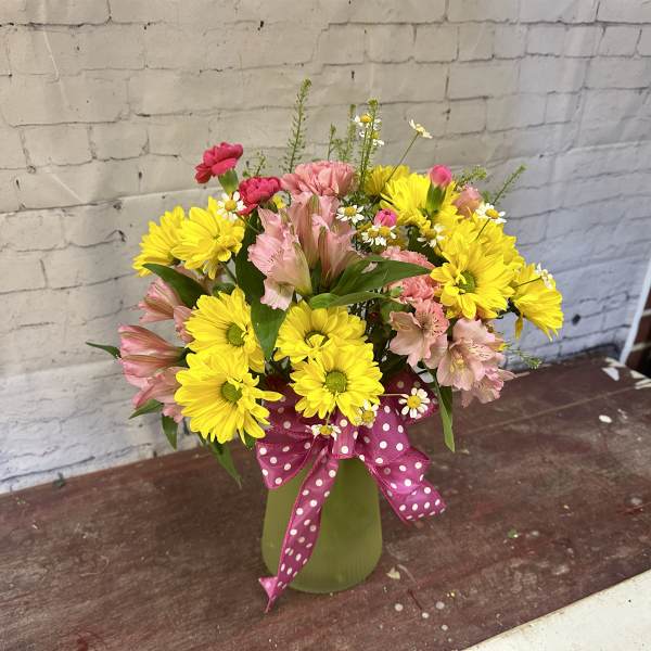 Bouquet of yellow daisies and pink alstroemeria in a green vase with a pink polka-dot ribbon