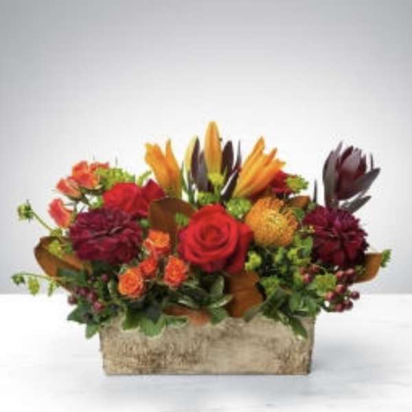 Mixed bouquet with red, orange, and burgundy flowers in a rectangular container