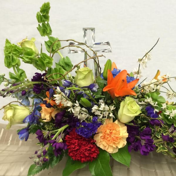 Colorful mixed flower arrangement with roses, lilies, and carnations around a clear glass cross
