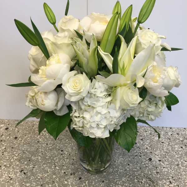 White floral bouquet in a clear glass vase with lilies, roses, and hydrangeas