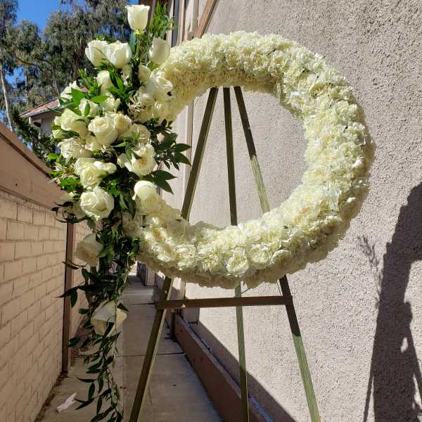 Large white floral wreath on an easel with roses and carnations