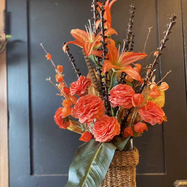 Orange floral arrangement in a tall woven vase