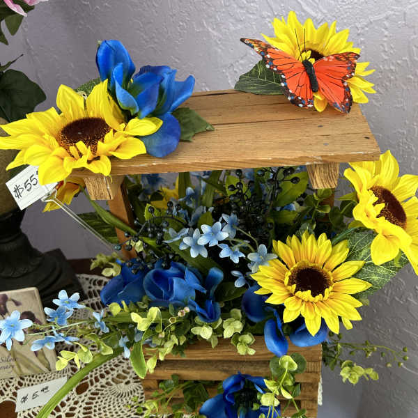 Wooden tiered floral display with sunflowers, blue flowers, and a butterfly