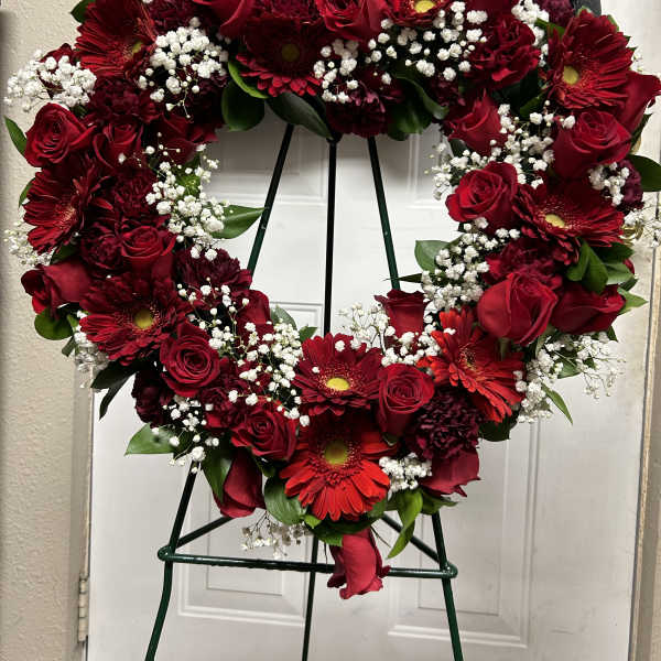 Heart-shaped wreath of red roses and gerbera daisies on a stand