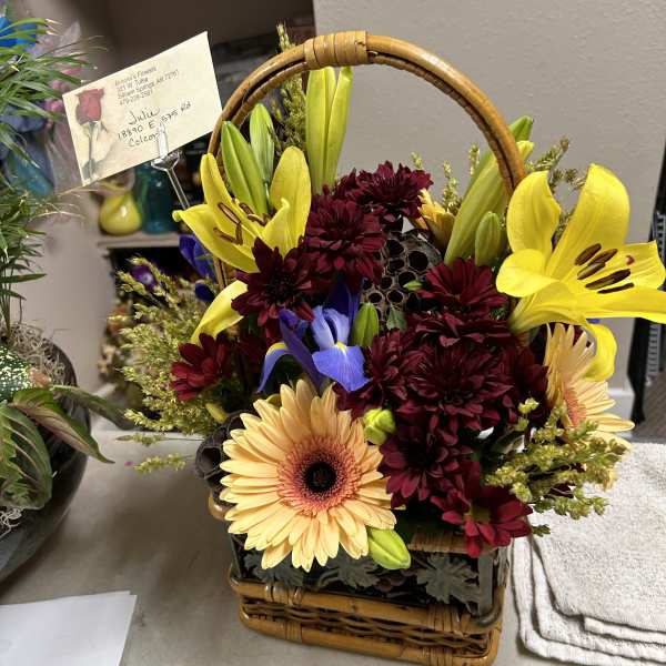 Basket arrangement with yellow lilies, burgundy mums, and peach gerbera daisies