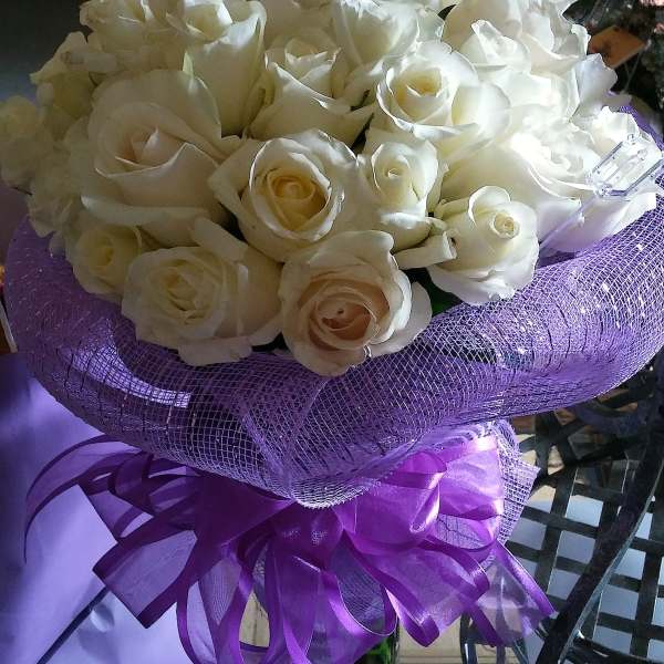 Bouquet of white roses wrapped in purple mesh with a ribbon