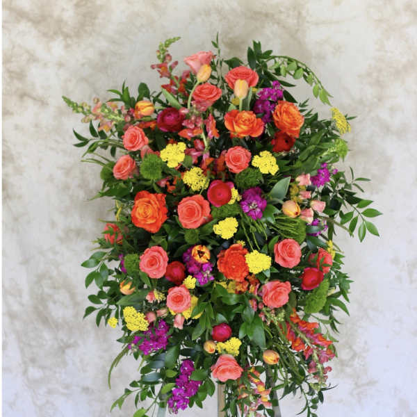 Bright standing spray of orange roses, yellow blooms, and pink and purple flowers on an easel