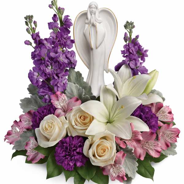 Purple and pink floral arrangement with white lilies and roses around an angel figurine