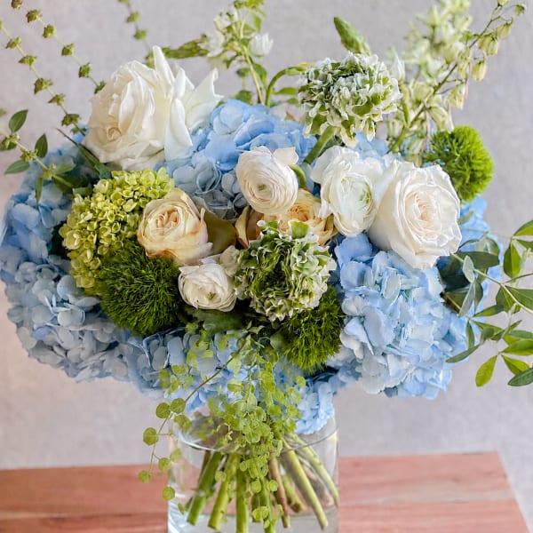 Blue hydrangeas and white roses arranged in a clear glass vase