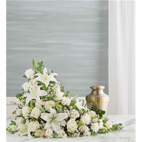 White floral funeral spray with lilies and roses beside a brass urn