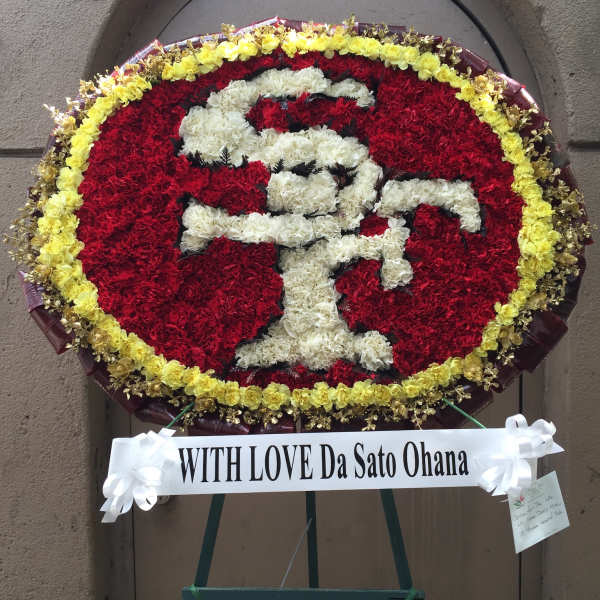 Large red and white floral standing wreath on an easel with a ribbon banner