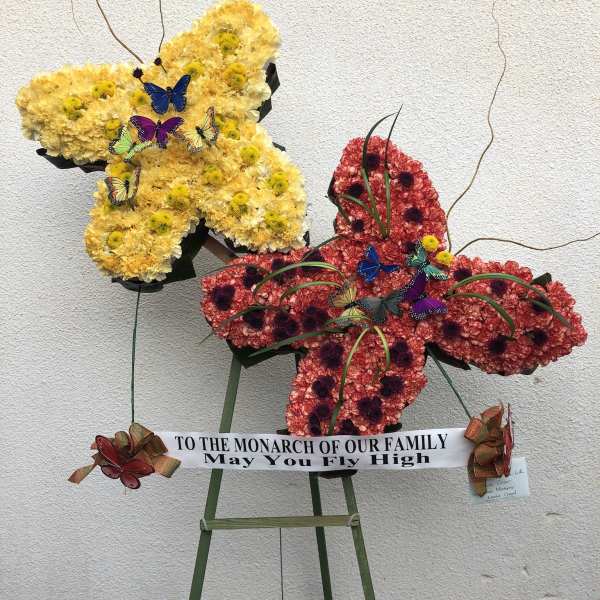 Butterfly-shaped floral display in yellow and red with a memorial ribbon
