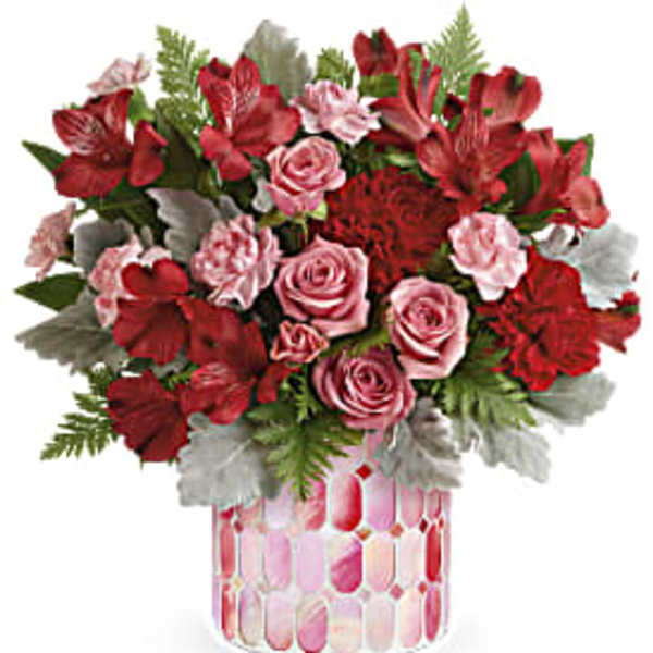 Red and pink flower arrangement in a patterned glass vase