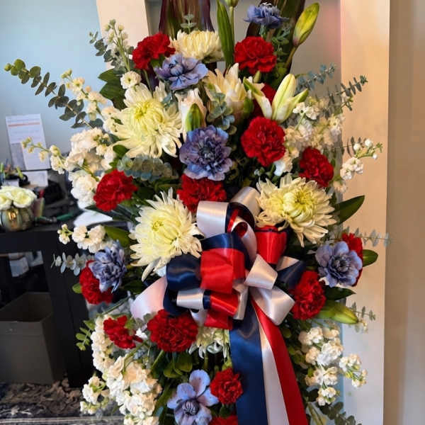 Standing floral spray with red, white, and blue flowers and a ribbon bow