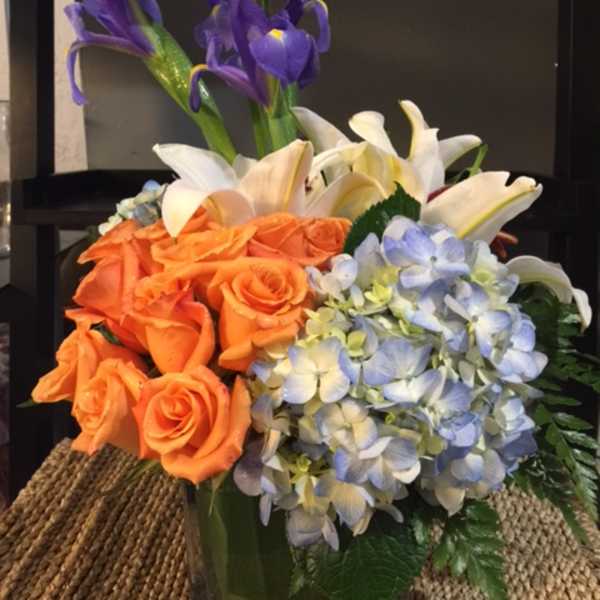 Bouquet of orange roses, white lilies, blue hydrangeas, and purple irises