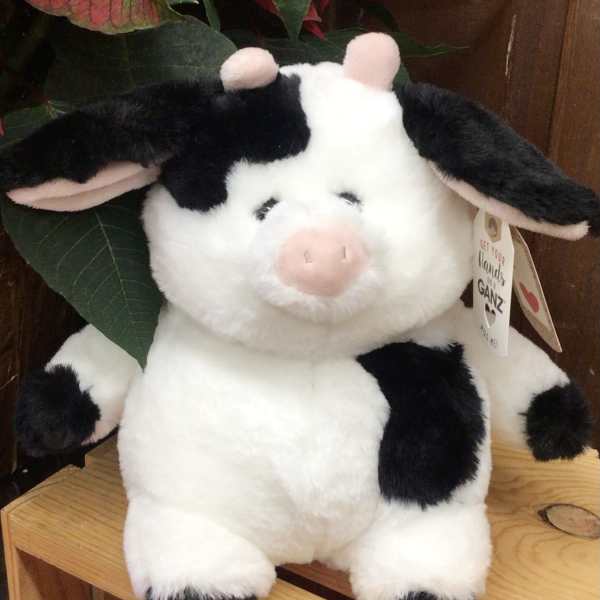 Plush black-and-white cow toy sitting on a wooden shelf