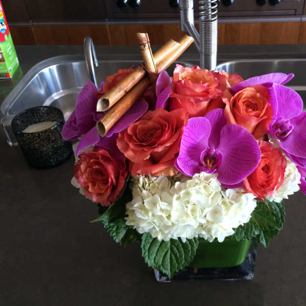 Bouquet of orange roses, purple orchids, and white hydrangeas in a square vase