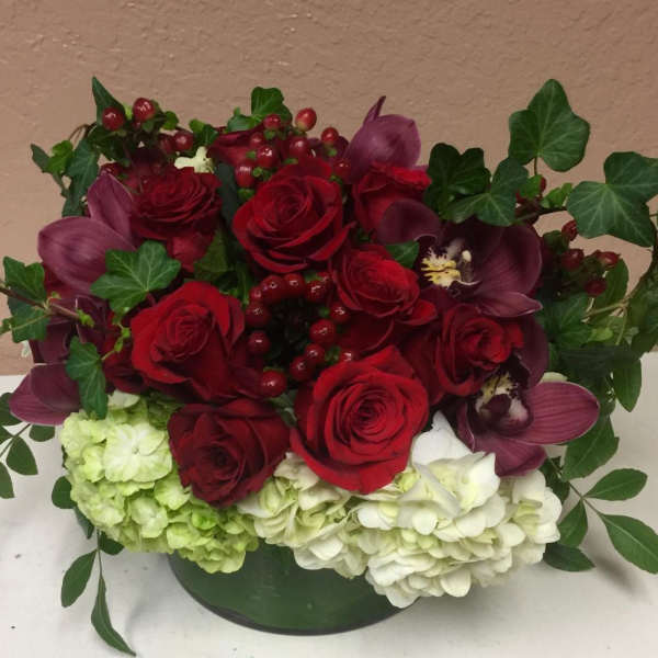 Red roses and purple orchids arranged with hydrangeas in a low container