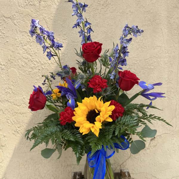 Bouquet of red roses, sunflowers, and blue flowers in a glass vase