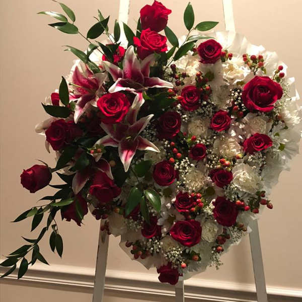 Heart-shaped floral wreath with red roses and white lilies on an easel