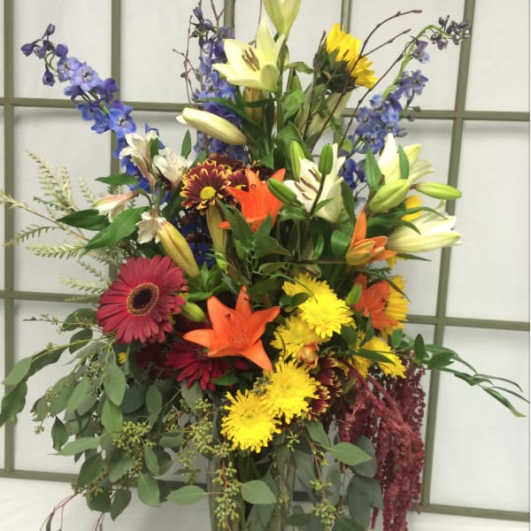 Tall mixed bouquet in a glass vase with lilies, gerberas, and blue flowers
