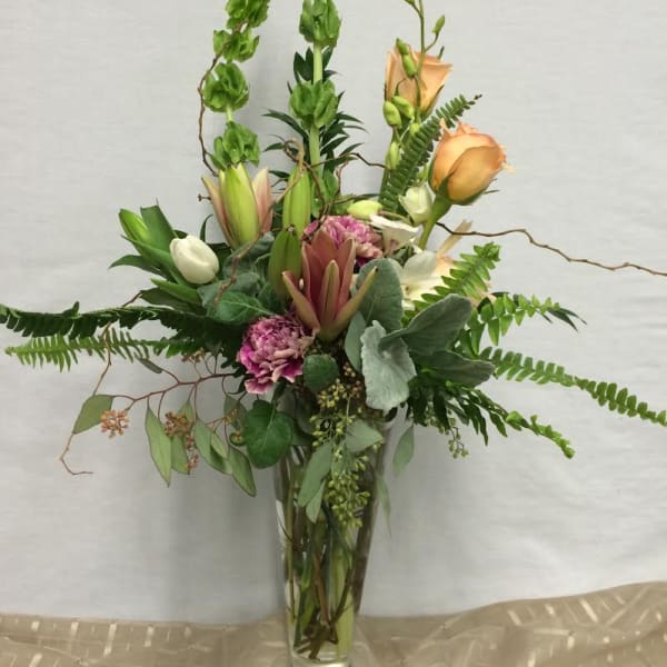 Tall mixed floral arrangement in a clear glass vase with peach roses and pink blooms