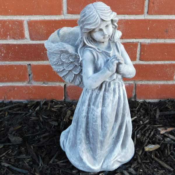 Gray angel statue standing against a brick wall