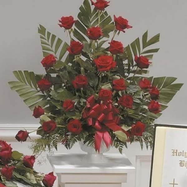 Tall arrangement of red roses with a red ribbon on a white pedestal
