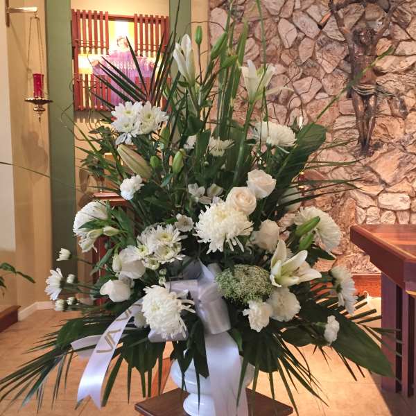 Tall white floral arrangement in a white vase with a ribbon bow